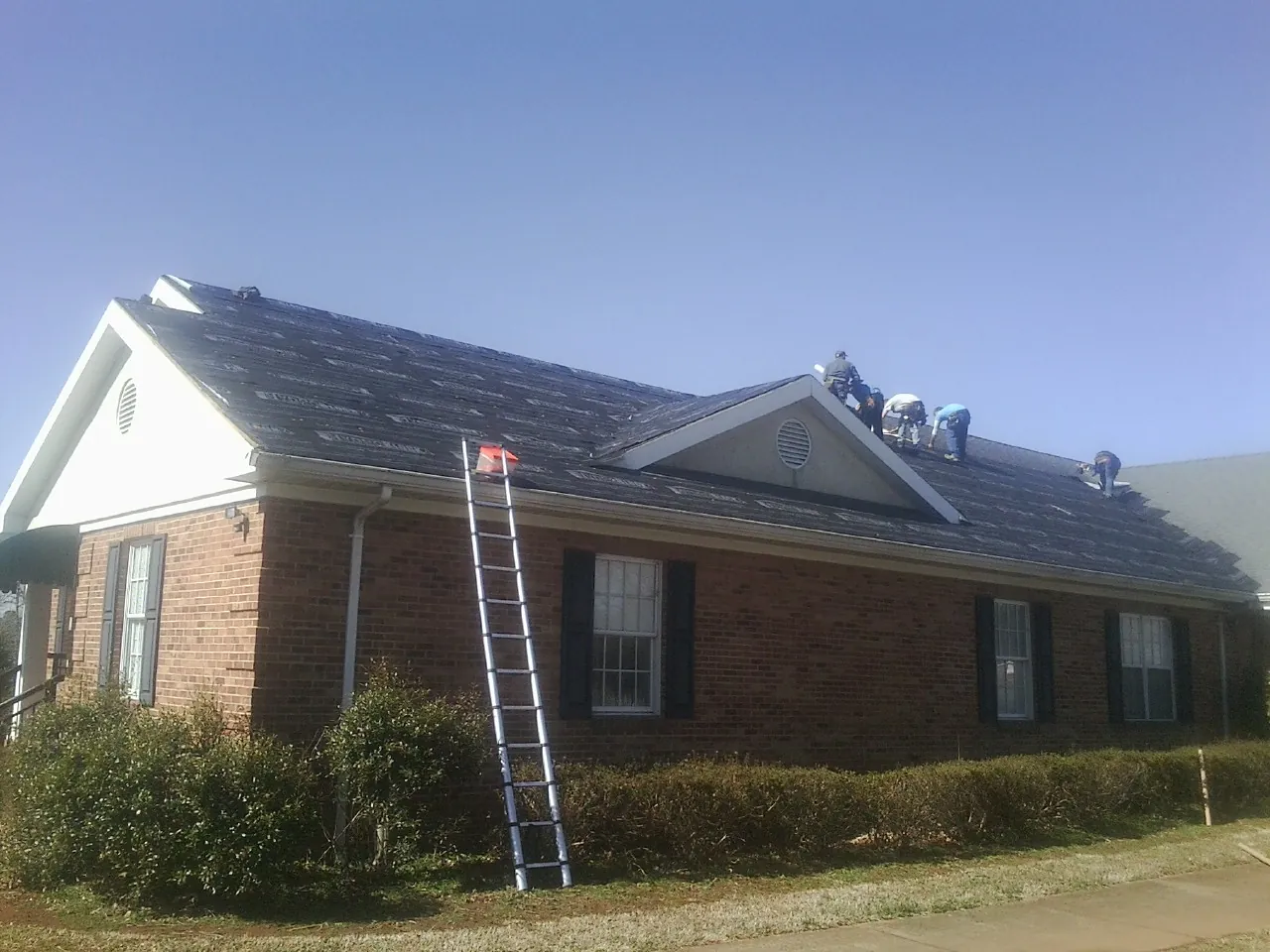 Crew tearing shingles off a brick ranch roof with a ladder set — Emergency Roof Repair work by our crew in Modesto