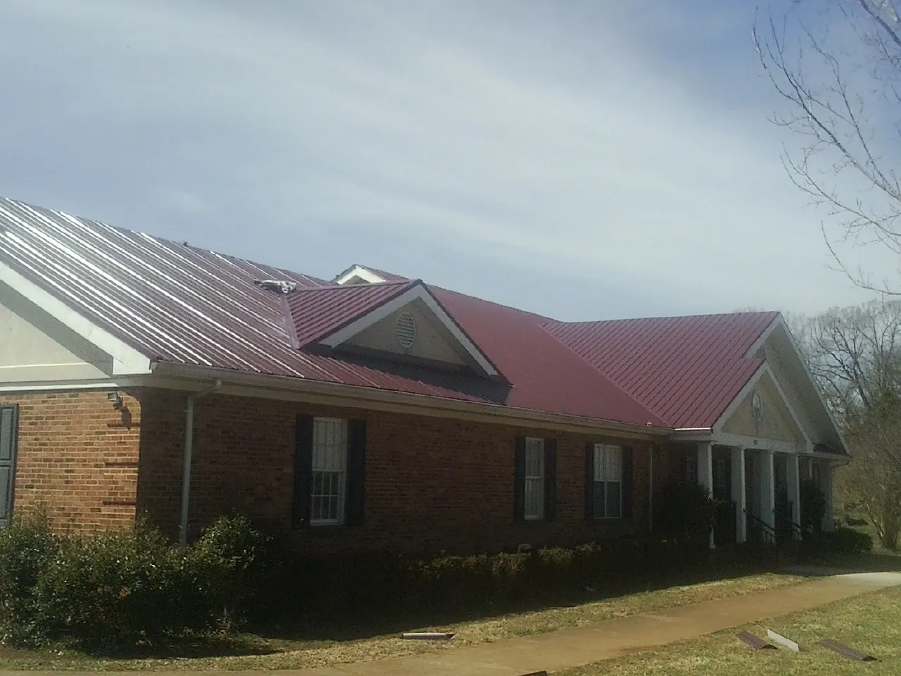 Red metal roof with gabled entries on a long brick building, from a Hail Damage Roof Repair job in Modesto