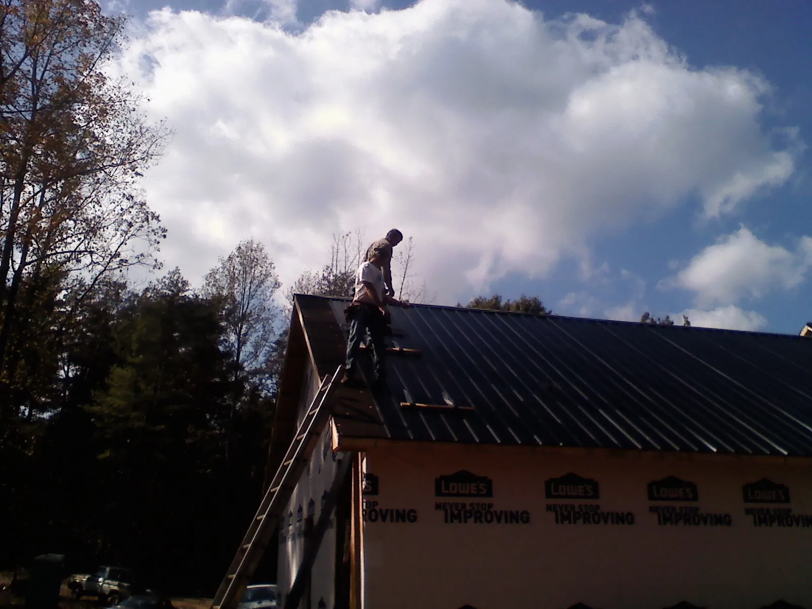 Roofer fastening dark metal panels high against a cloudy sky, from a Roof Inspection job in Modesto